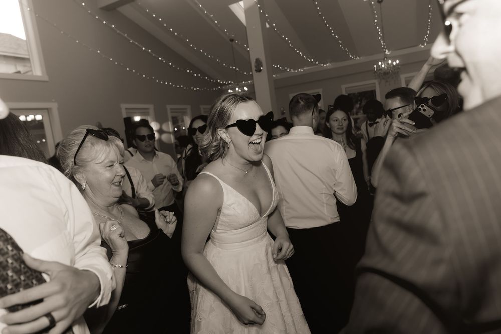 Guests dancing at a wedding reception in black and white, woman in sunglasses enjoying the celebration.