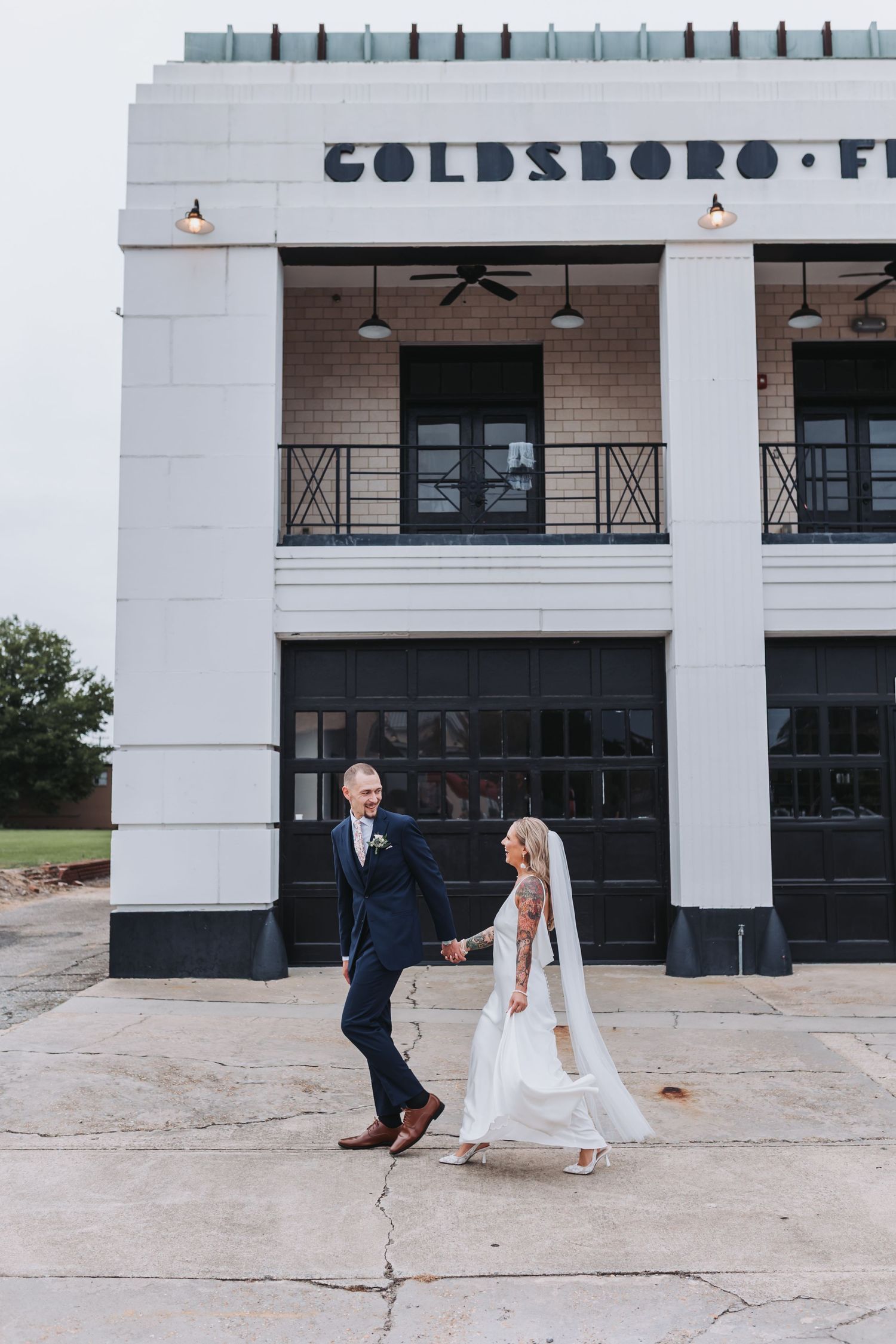 Two brides in white gowns pose elegantly at a bar with warm orange walls and string lights.