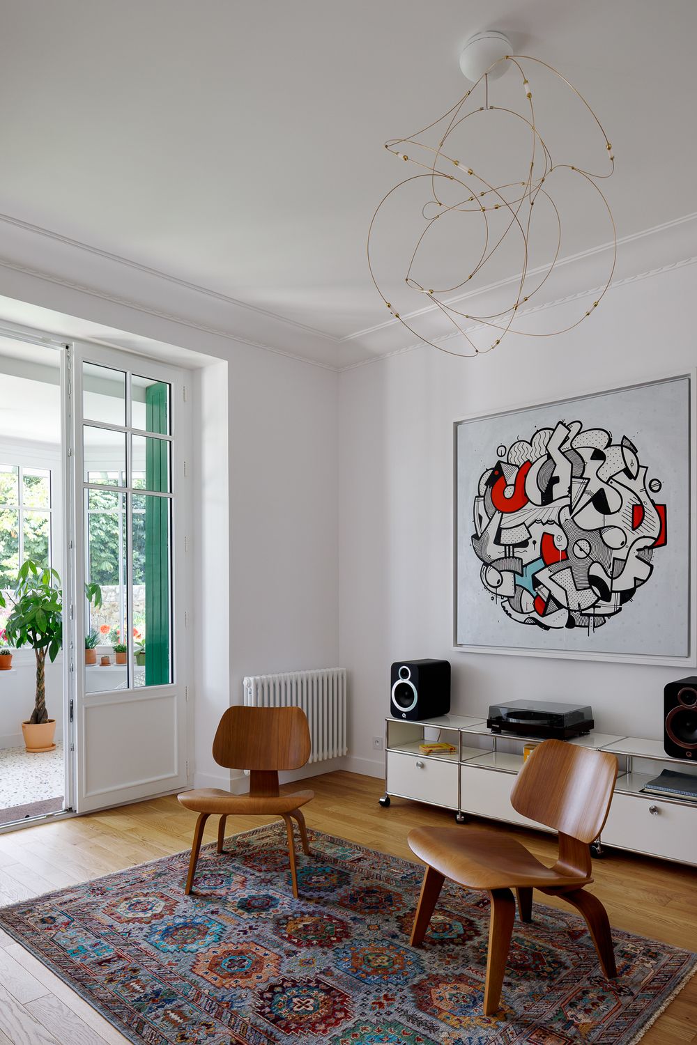 Salon contemporain avec des fauteuils Eames, des œuvres d'art abstraites et un lustre décoratif en fil métallique.