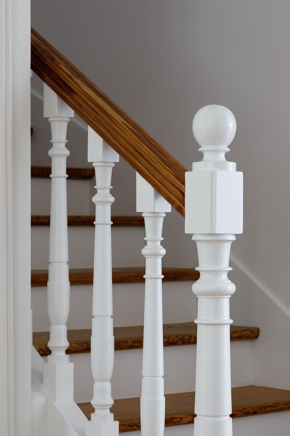 Rampe d'escalier classique en bois peint en blanc, avec des barreaux décoratifs et un poteau de départ surmonté d'une boule.
