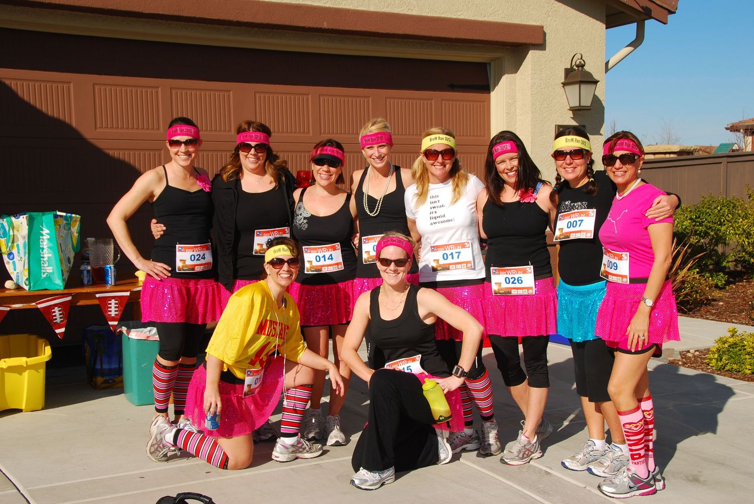 Group of women in bright pink tutus and 80s-style running costumes posing together before a fun run race.