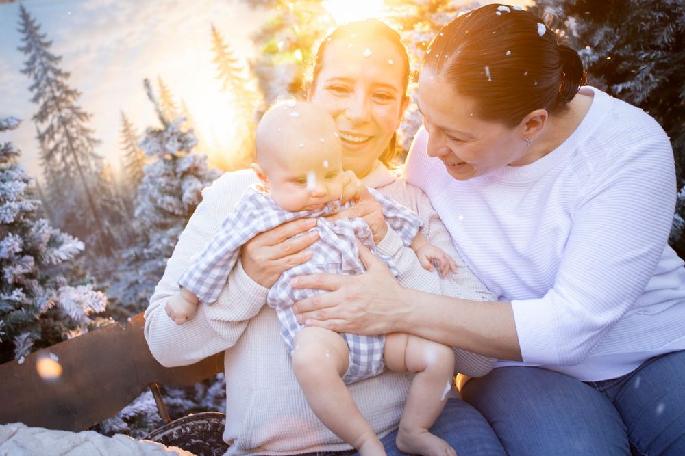 Happy family with baby enjoying a snowy winter outdoor photo session with sunlit snow-covered trees.