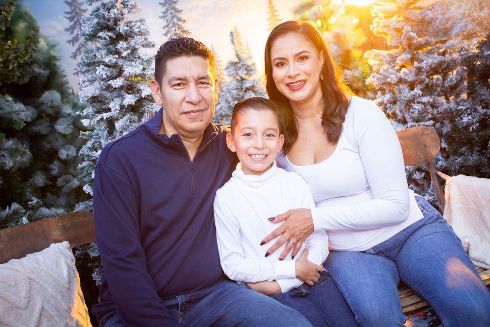 Family of three poses together near snowy trees in a warm holiday outdoor portrait setting.