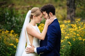 Bride and groom share an intimate moment surrounded by yellow wildflowers, with bride in white gown and groom in navy suit.