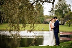 Bride and groom share a romantic moment by a serene pond surrounded by lush greenery on their wedding day.