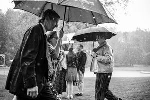 Black and white photo of people walking in heavy rain with umbrellas at an outdoor event.