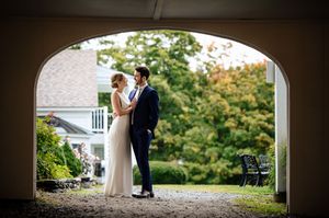 Bride and groom share a romantic moment framed by an elegant stone arch at a lush garden wedding venue.