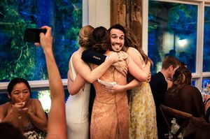 Guests sharing a warm group hug at a wedding reception, with others smiling and celebrating in the background.