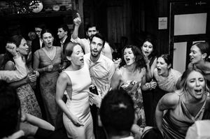 Black and white photo of joyful wedding guests dancing and celebrating together at a lively indoor reception party.