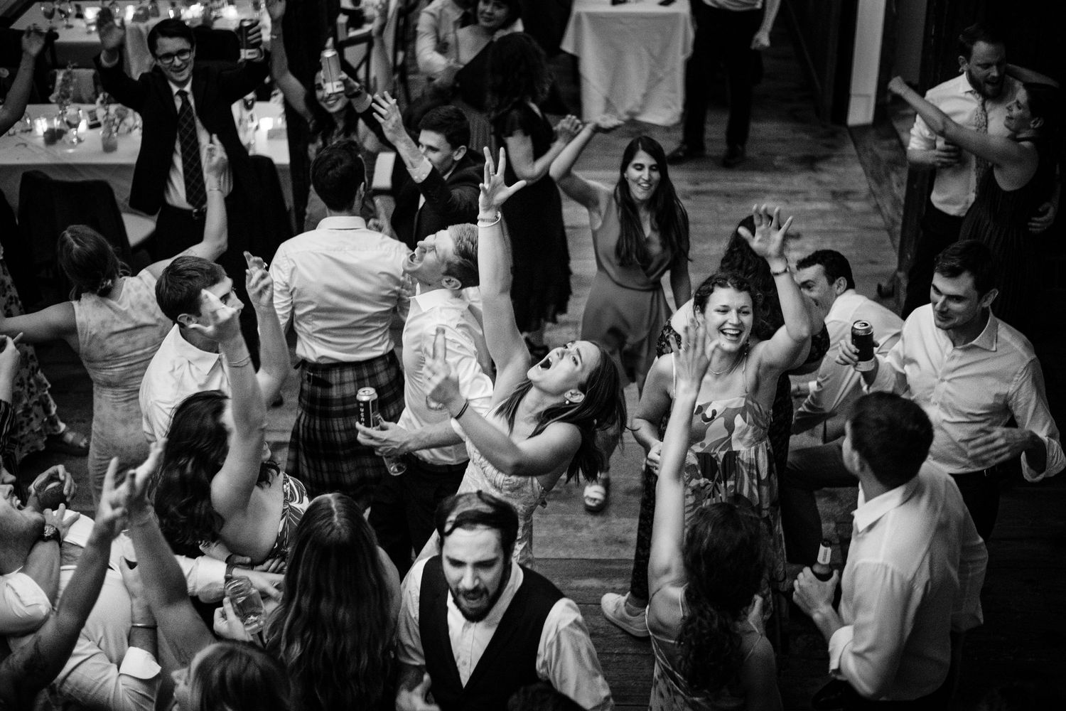 Black and white photo of joyful wedding guests dancing energetically at a lively reception party.