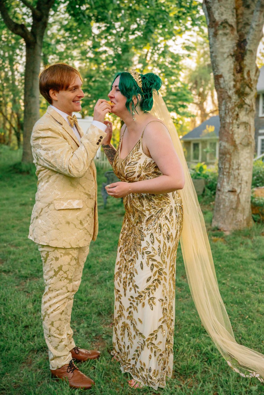 Couple in gold wedding attire sharing a sweet moment outdoors, bride in gold leaf gown with green hair and veil.