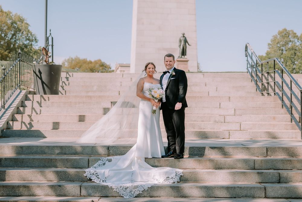 Bride and groom pose on grand stone steps in front of a monument on their wedding day.