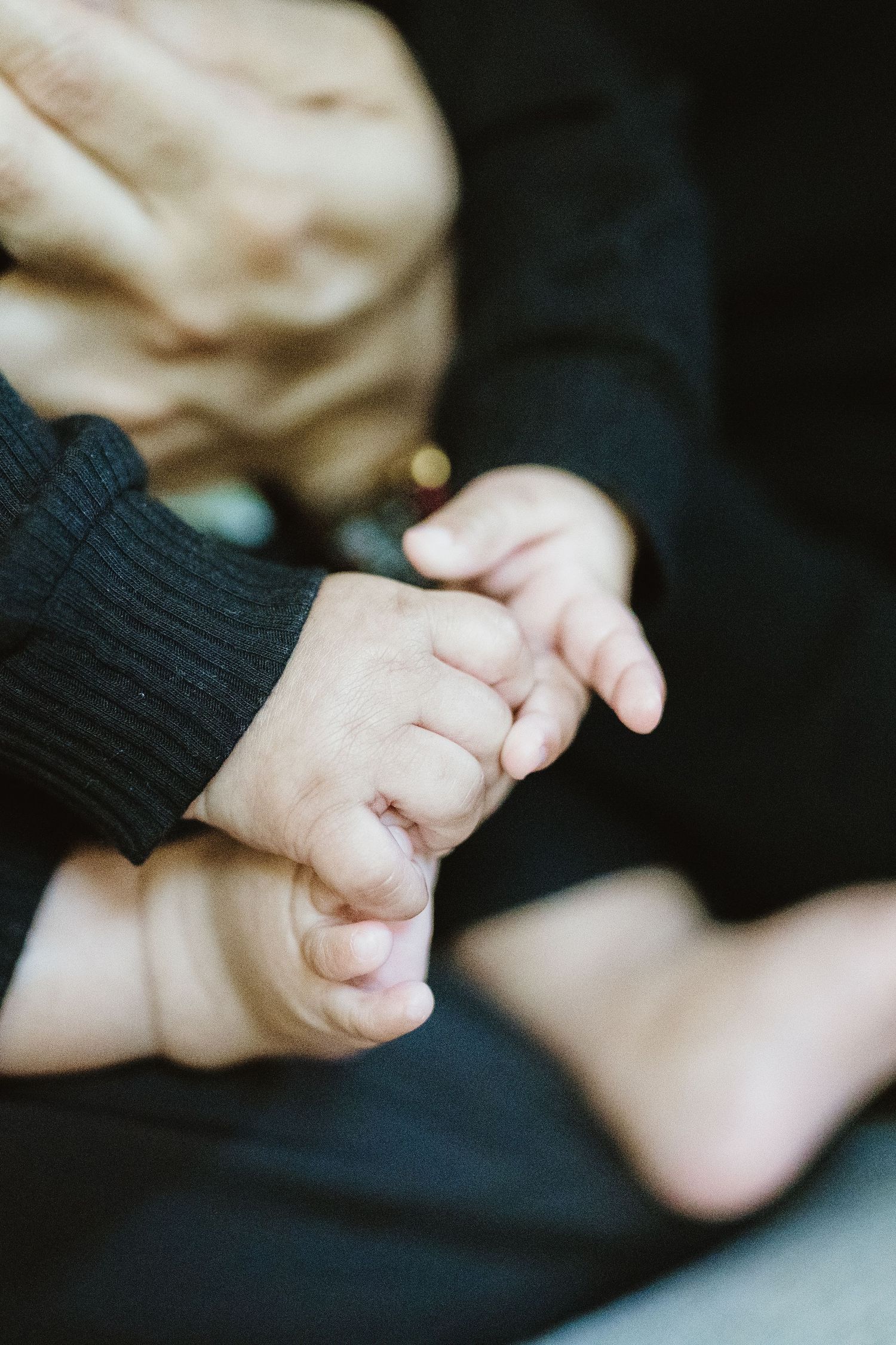Adult hand gently holding a newborn baby's tiny feet and hands, close-up shot showing delicate skin details.