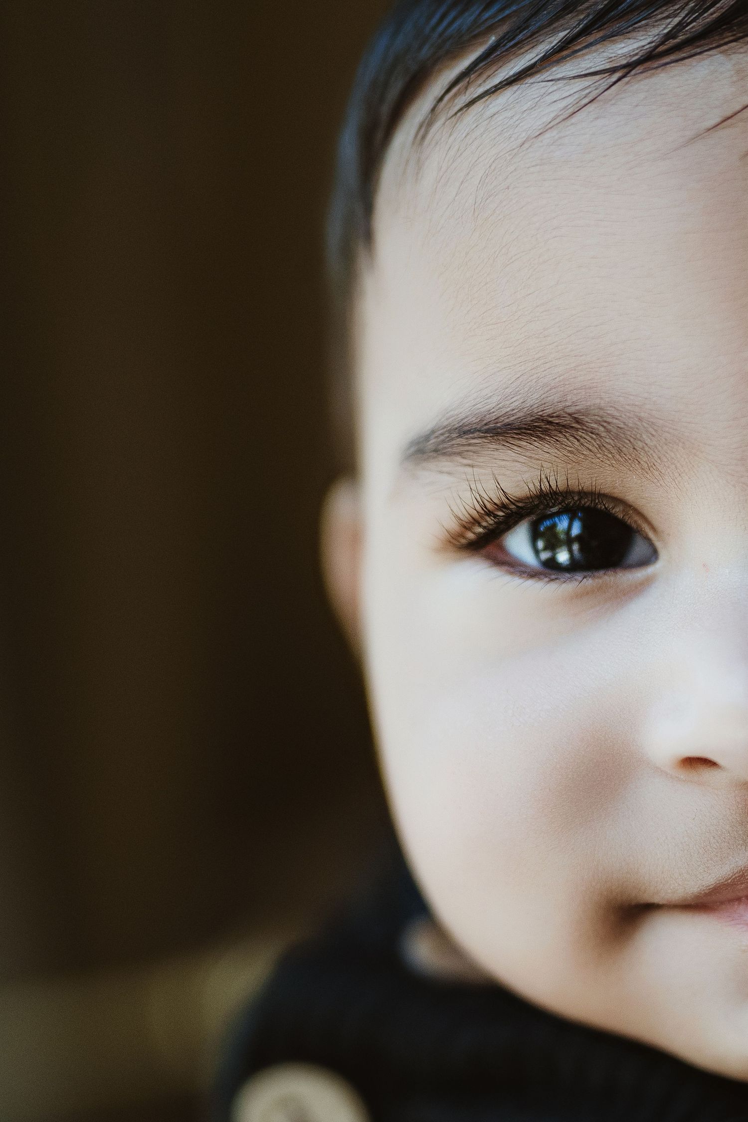 Close-up portrait of a baby with big brown eyes and long lashes, smiling softly in natural light.