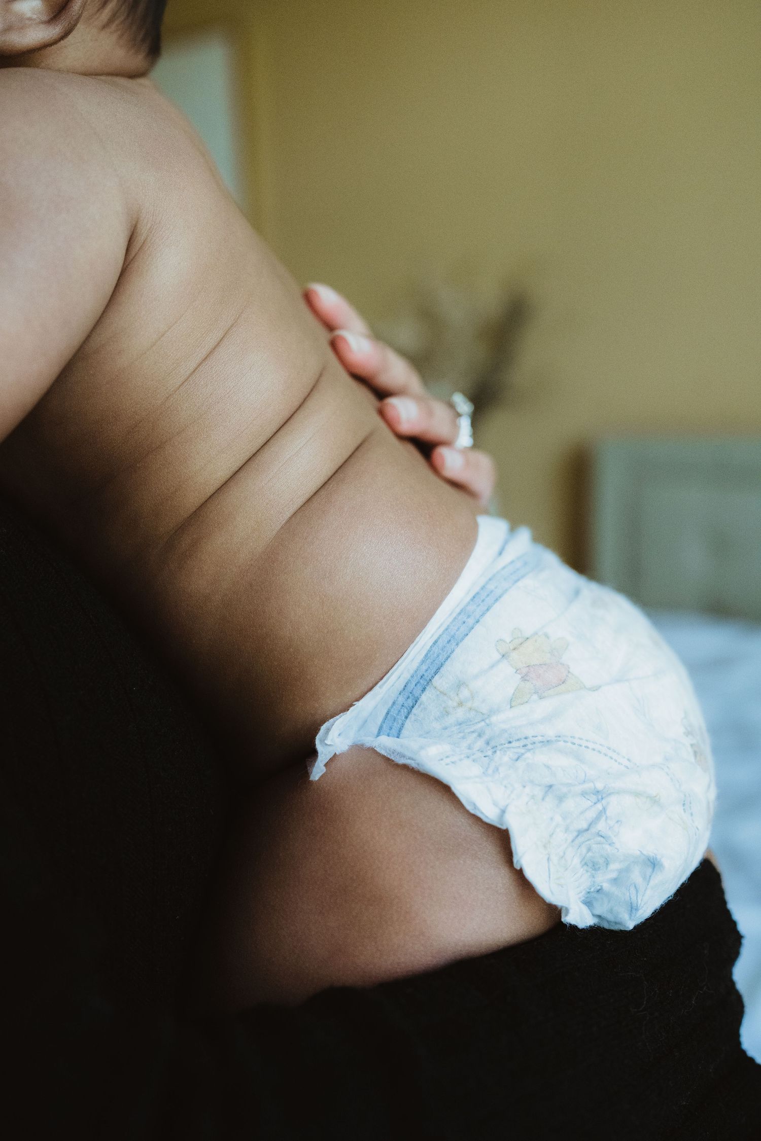 Close-up of a baby in a white diaper being held by an adult, showing chubby back and side rolls.