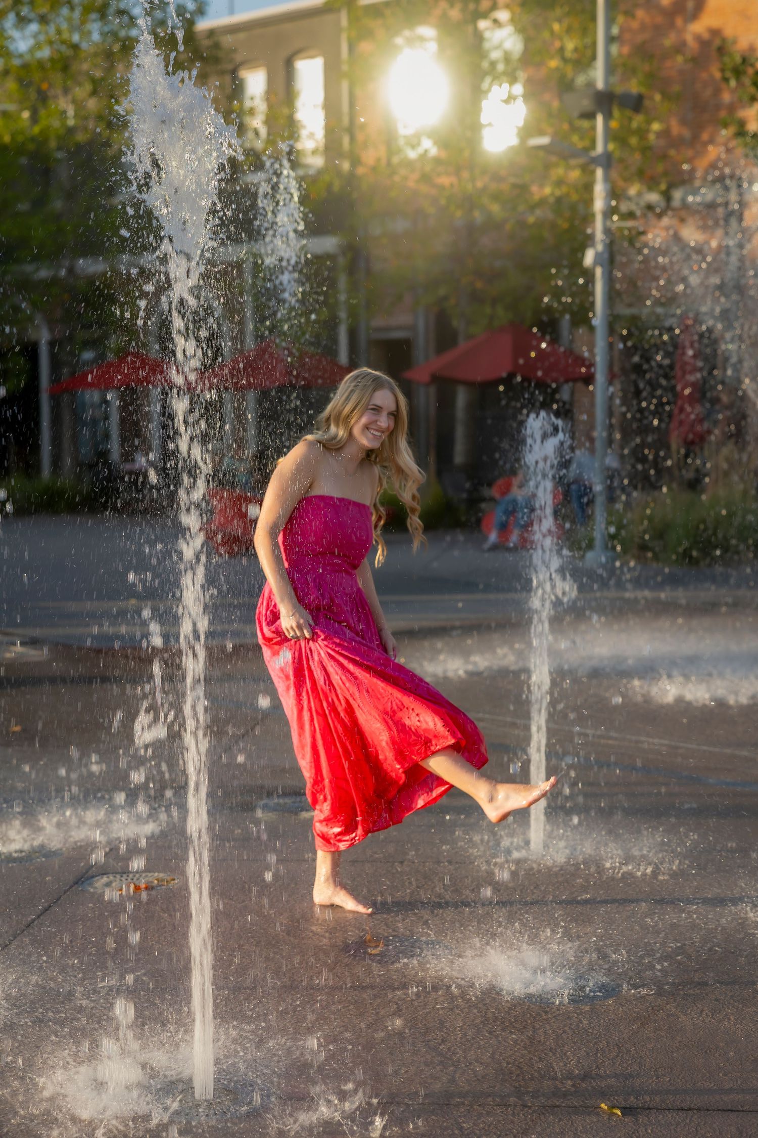senior girl wearing a pink dress barefoot splashing around on a splash pad