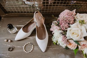 Bridal accessories flat lay including wedding shoes, perfume, and bouquet.