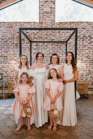 Bride posing with her bridesmaids and flower girls in neutral tones inside the venue.