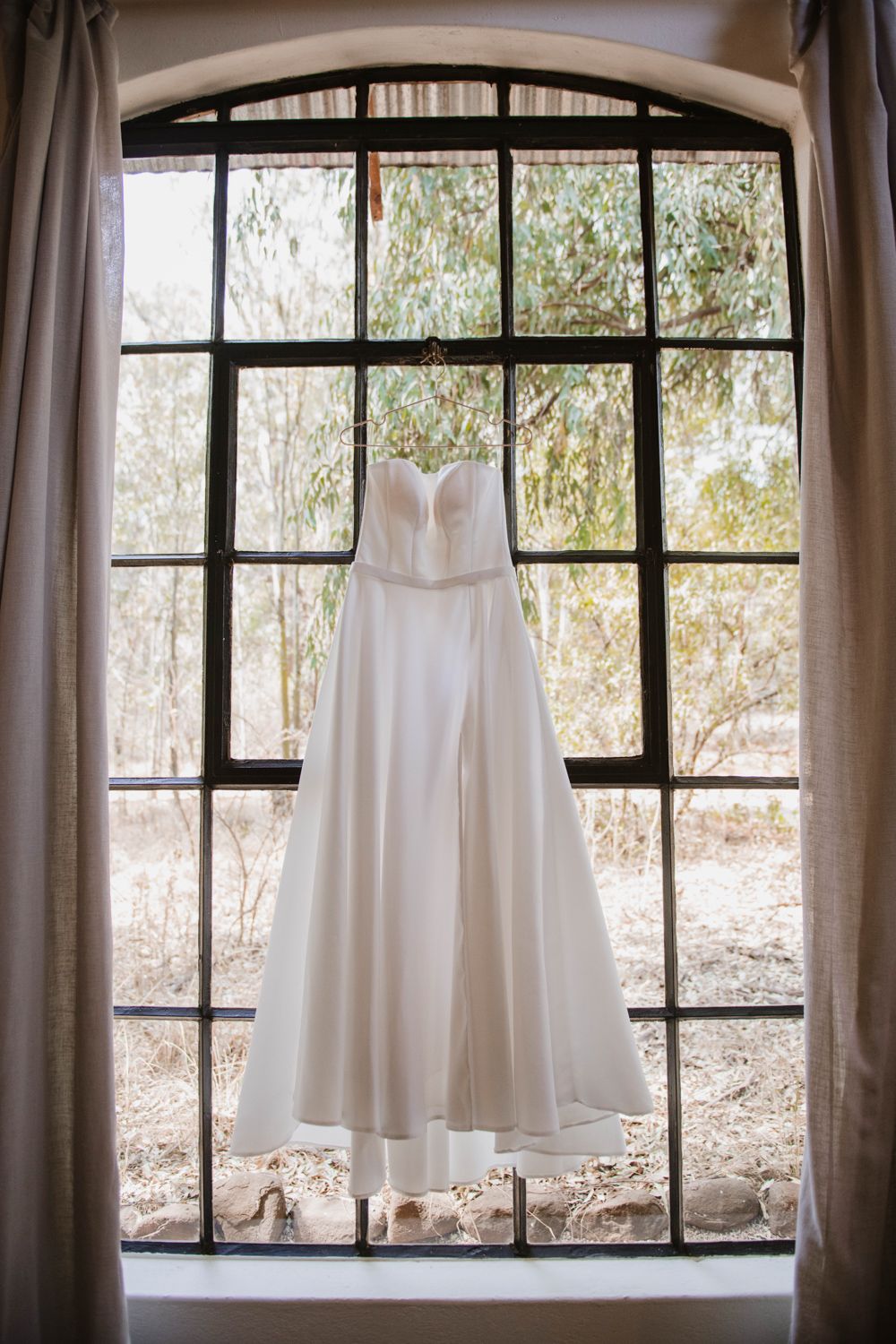 Wedding dress hanging in front of a large industrial window with natural light.
