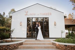 Wide shot of the couple standing on the steps of a white barn wedding venue.