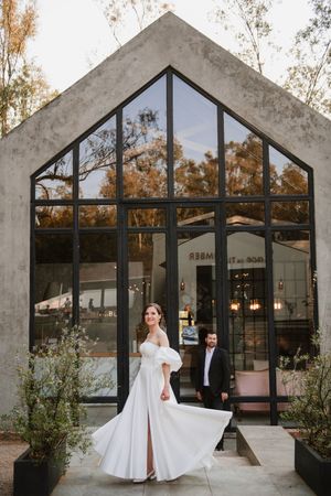 Wide shot of the newlyweds sitting together, framed by tall glass windows.