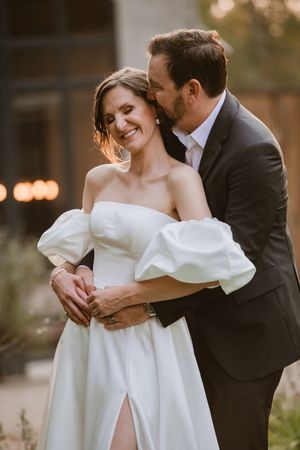 Couple standing close together with warm sunset light behind them.