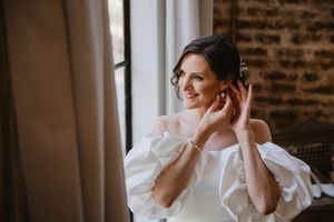 Smiling bride fixing her hair in a soft window-lit room.