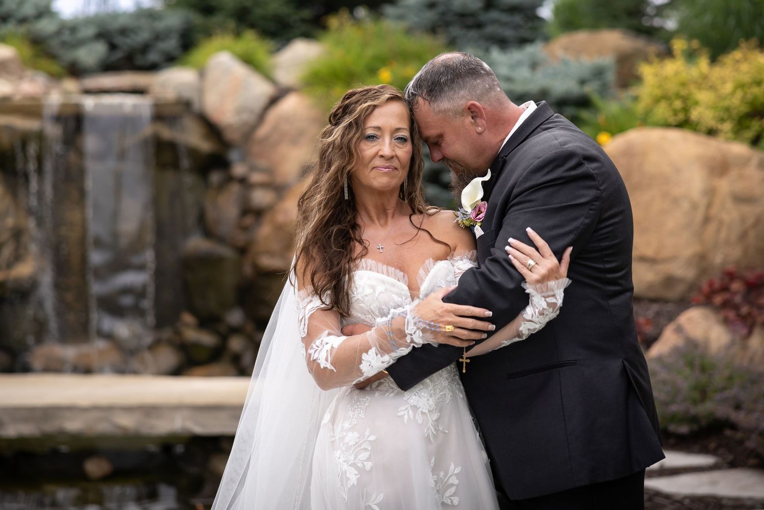 Couple shares romantic kiss by waterfront while holding colorful bouquet.