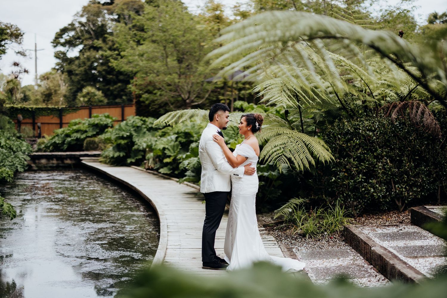 Elegant outdoor wedding ceremony setup with white chairs, floral arch, cherry blossoms, and umbrellas on a lush green lawn.