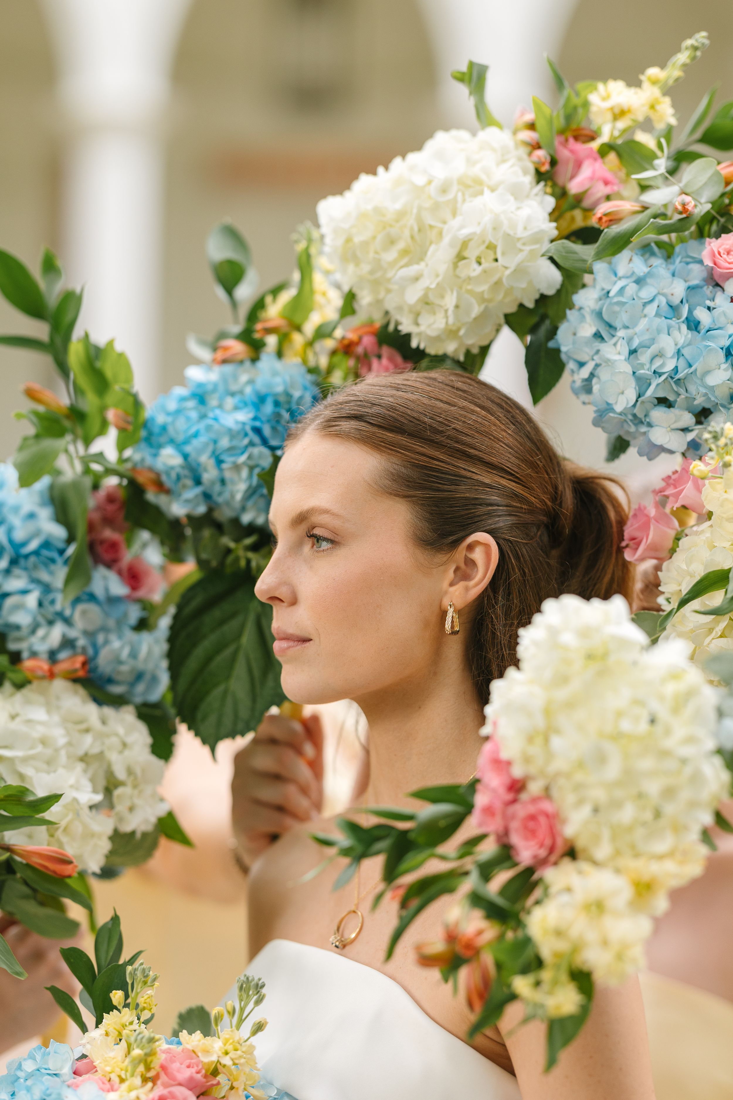Beautiful floral arrangement with white and blue hydrangeas, pink roses and greenery surrounds someone in a side profile pose.