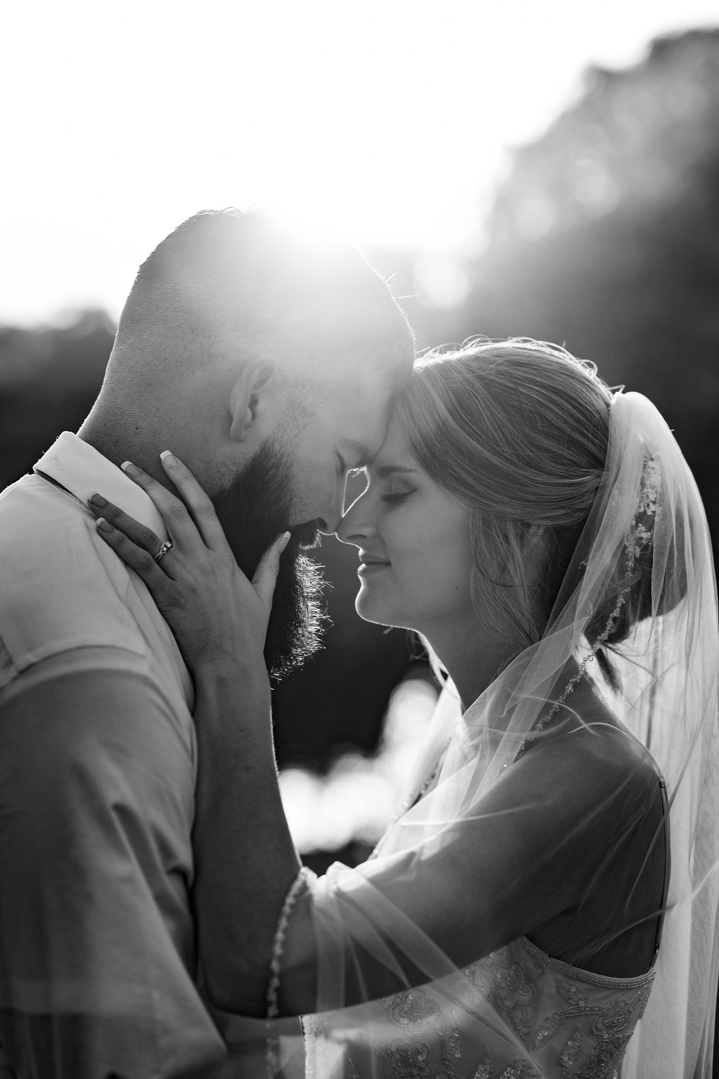 A backlit black and white portrait capturing a tender moment between newlyweds.
