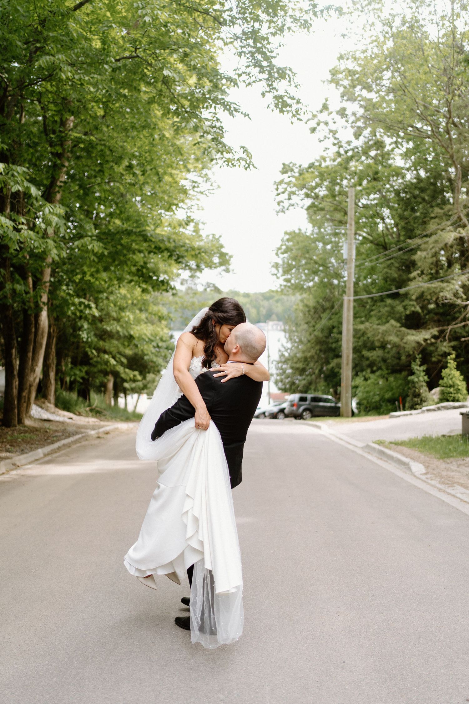 A romantic moment captured as a couple embraces on an empty tree-lined street at Windmere Resort-Muskoka Wedding Photographer