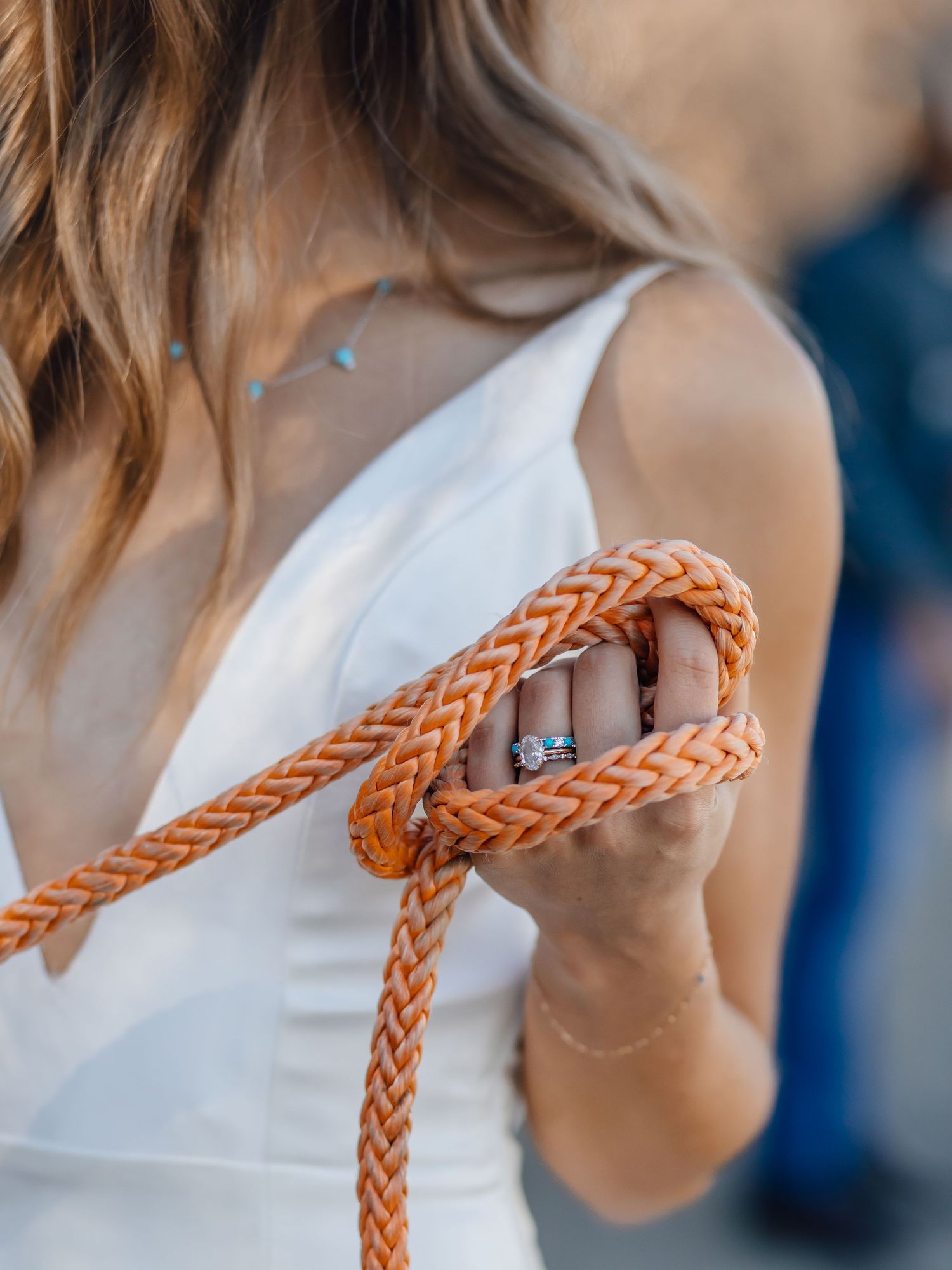 Close-up of hands holding an orange braided rope against a white dress with an engagement ring visible.