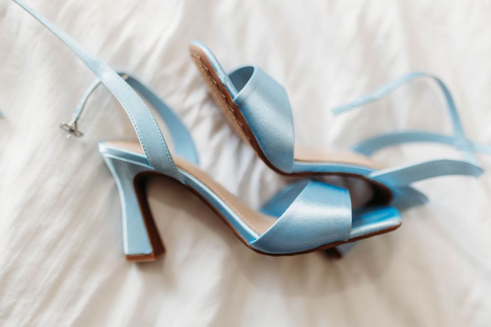 Delicate light blue satin strappy bridal heels with kitten heels displayed on a soft white fabric surface.
