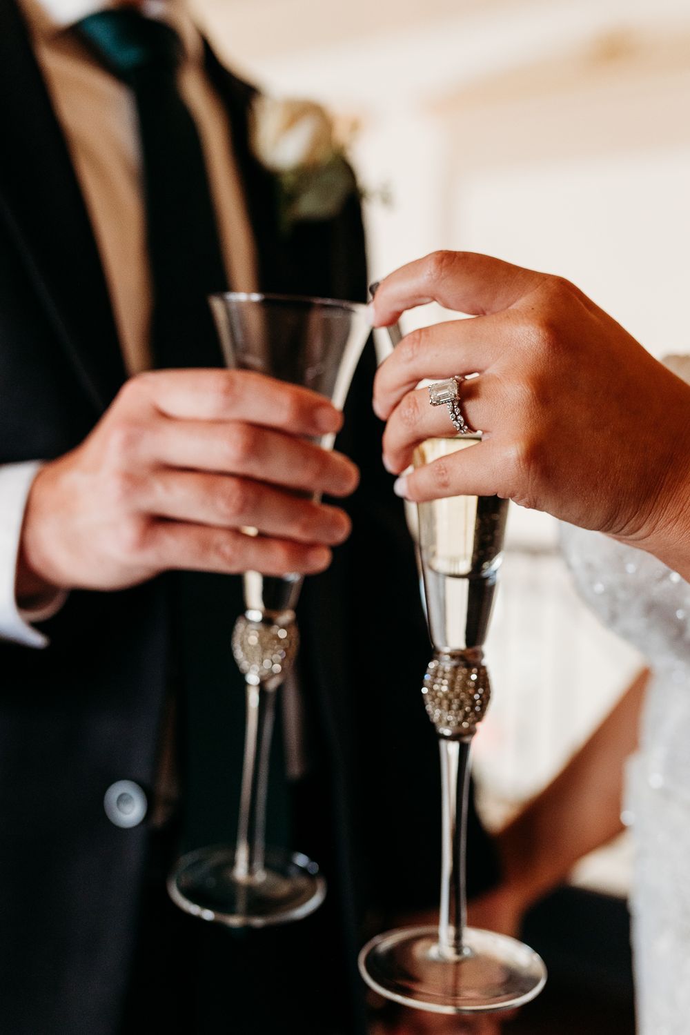 Bride and groom clinking decorative champagne flutes during wedding toast with diamond ring visible.