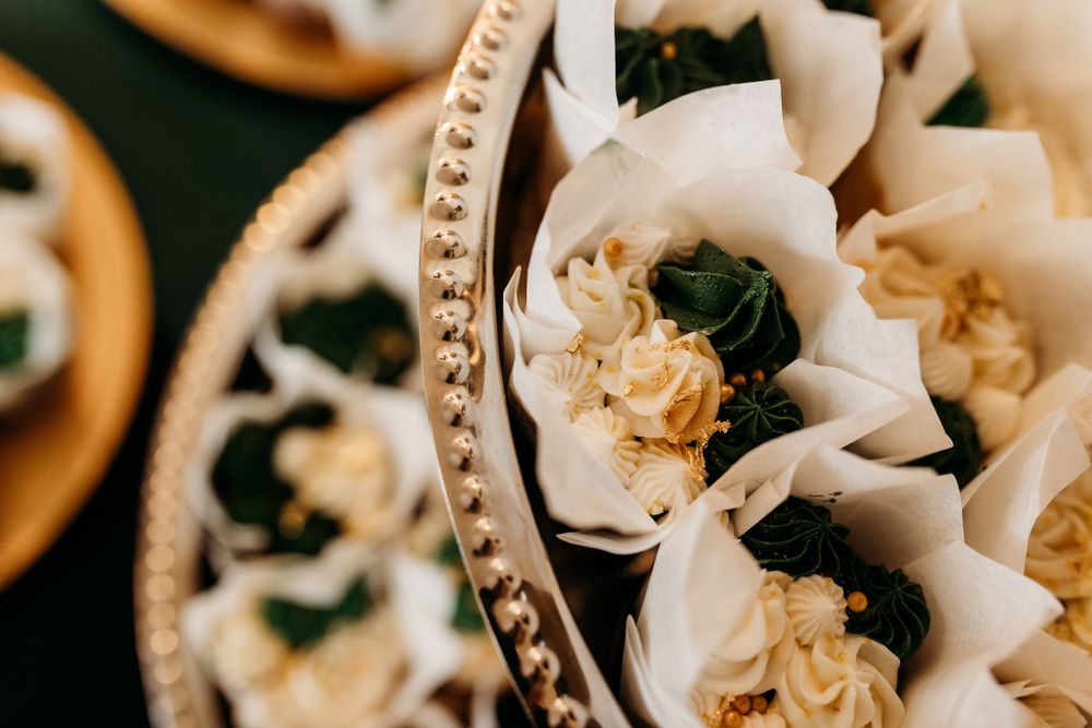 Close-up of elegant white paper-wrapped cupcakes with gold frosting on a decorative silver tray.