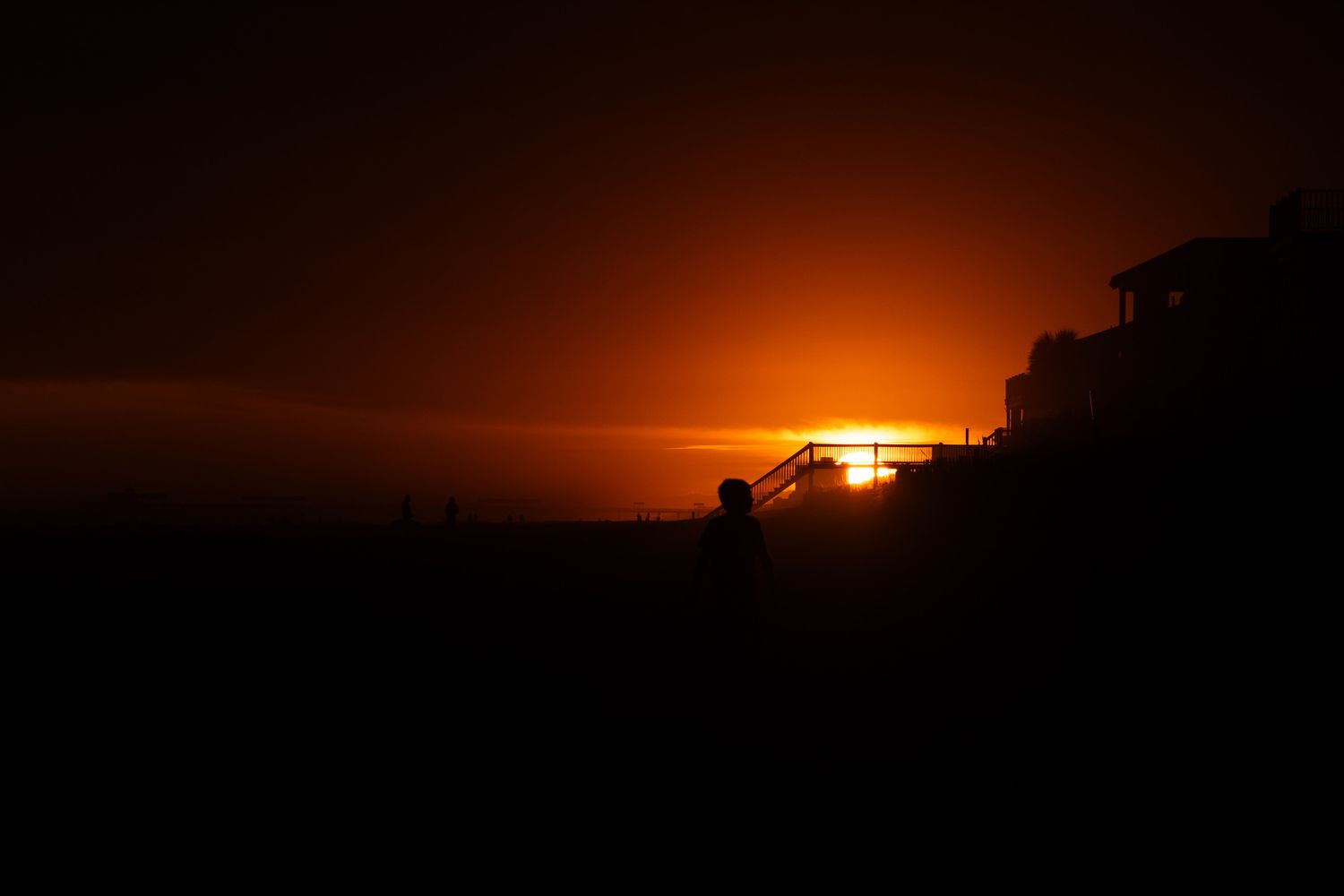 Dramatic orange sunset silhouettes against dark horizon creating a moody atmospheric landscape.