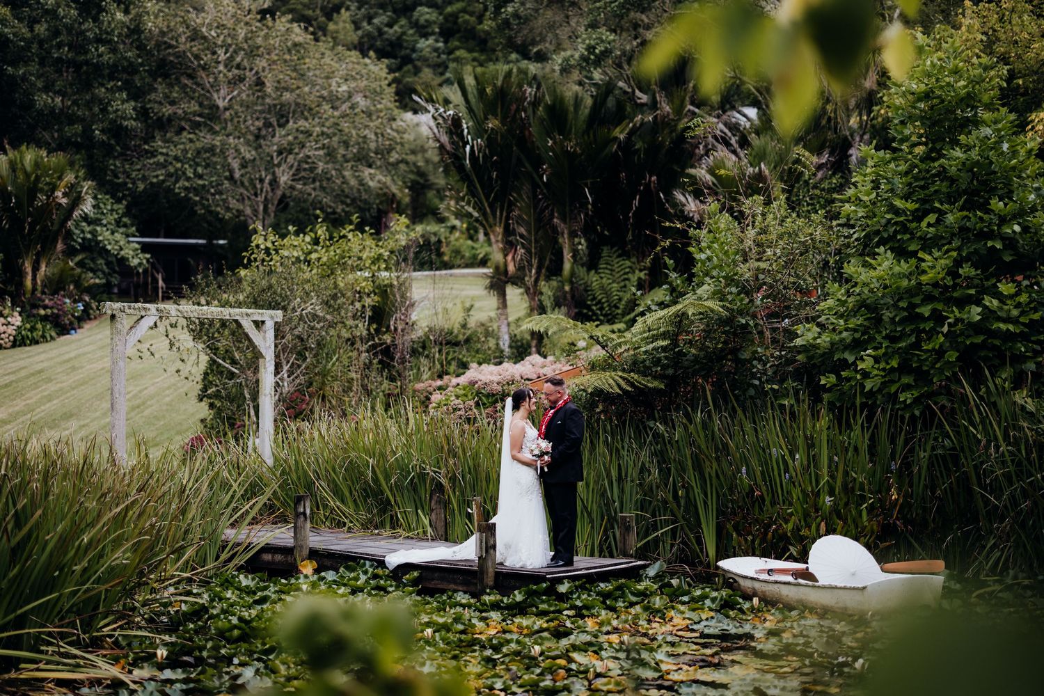 Wedding couple ascending sunlit garden stairs surrounded by lush greenery.