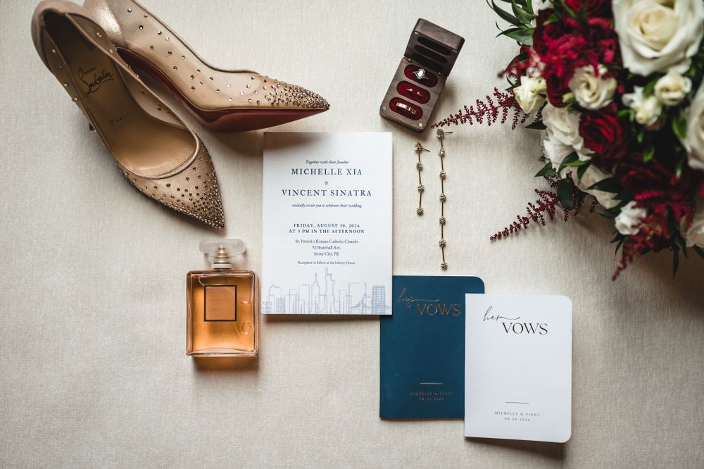 Wedding details flatlay with blush shoes, invitations, perfume and floral arrangements.
