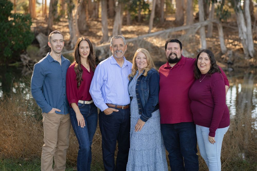 A group of people in coordinated burgundy and blue outfits pose together outdoors during golden hour.