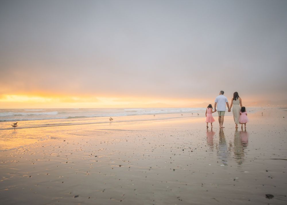Group of silhouettes walks together while sunset paints the sky orange on an expansive beach.