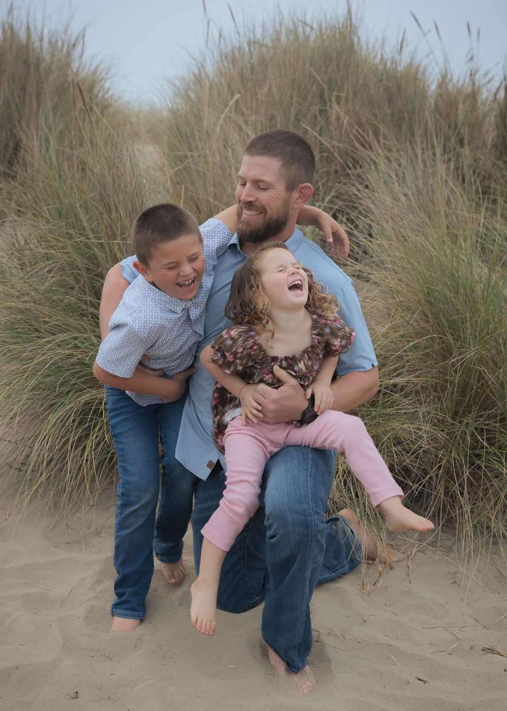 A joyful family moment captured in tall beach grass with everyone laughing together on the sand.
