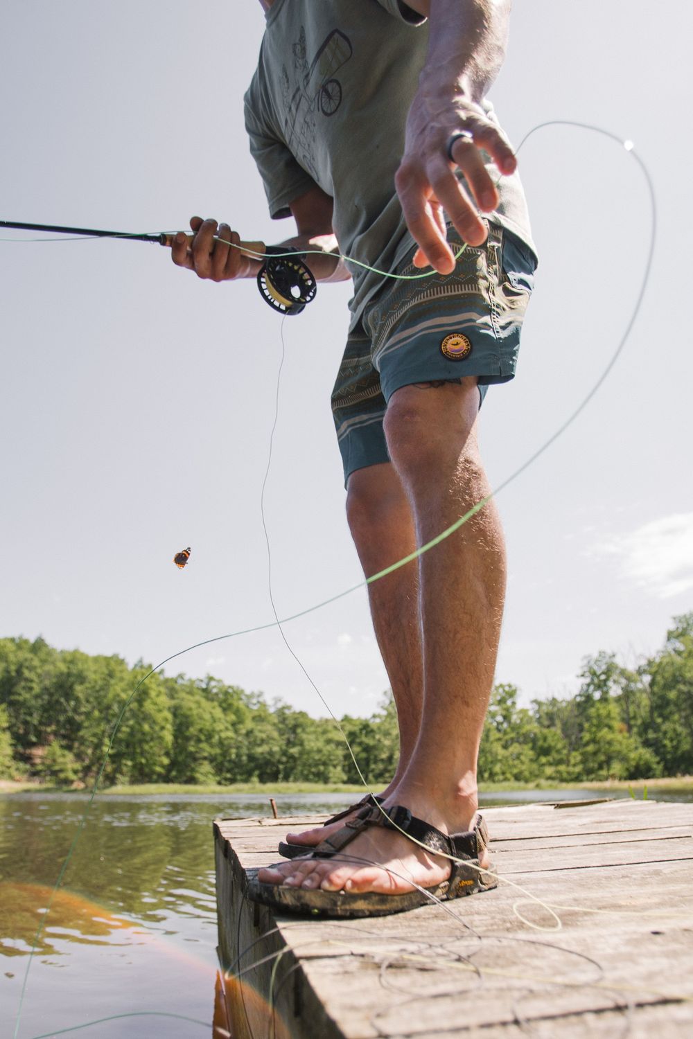 Person fly fishing from a wooden dock over calm waters on a sunny day.