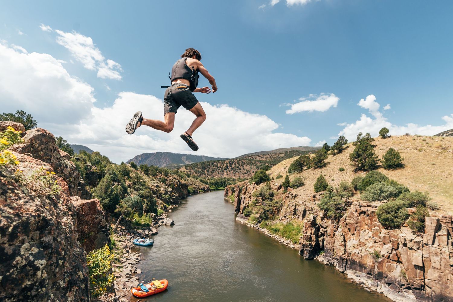 People jumping into a scenic mountain lake surrounded by cliffs on a sunny day.