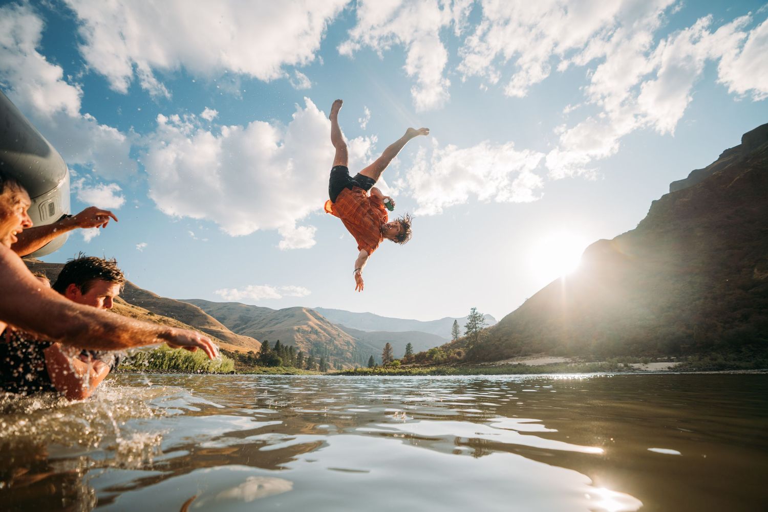 Panoramic view of people diving and splashing into a mountain lake with dramatic cliffs.