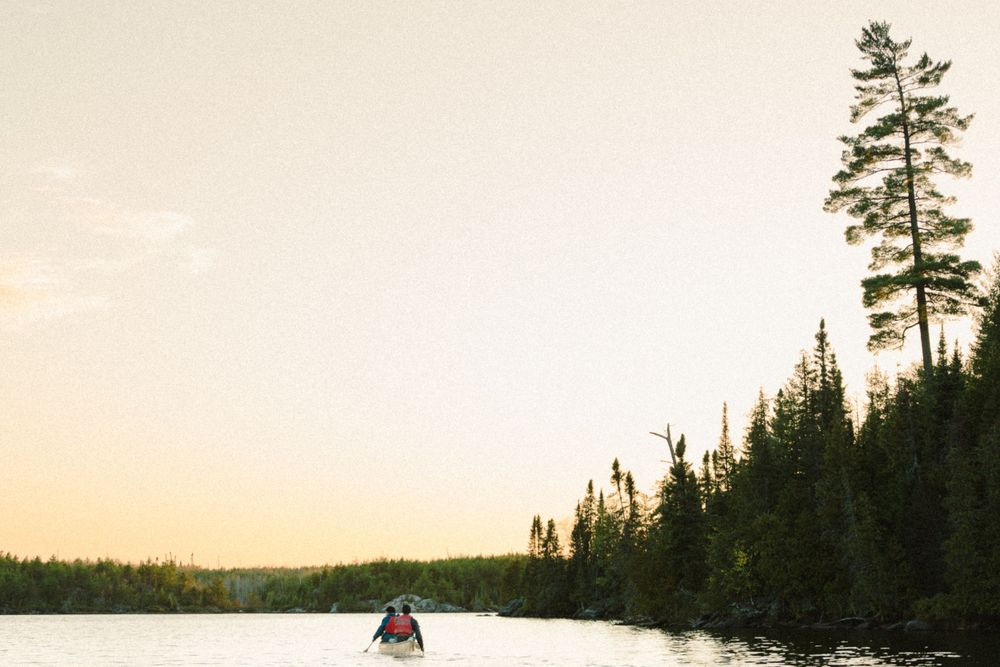Sunset over a serene lake surrounded by pine trees in a wilderness setting.