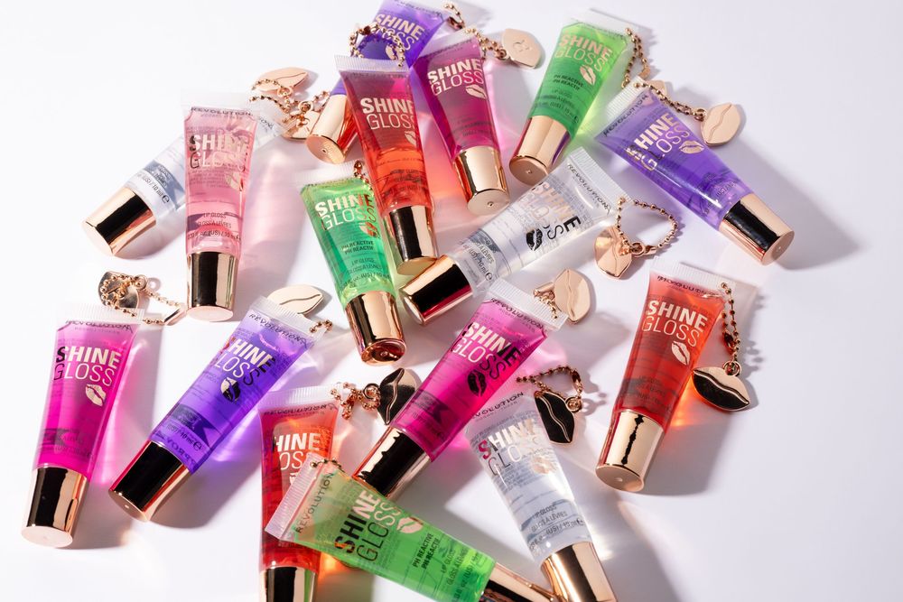 Collection of Victoria's Secret Shine Kiss lip glosses in assorted colors scattered on white background.