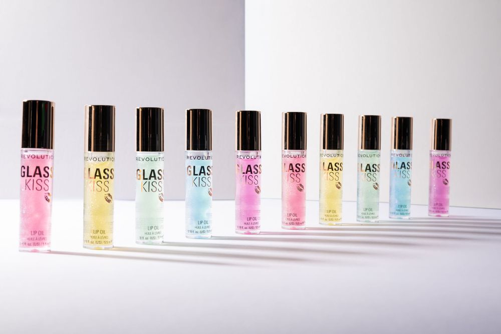 Array of colorful Glass Kiss roller lip glosses in pink, yellow, mint, and lavender shades displayed in a row on white surface.