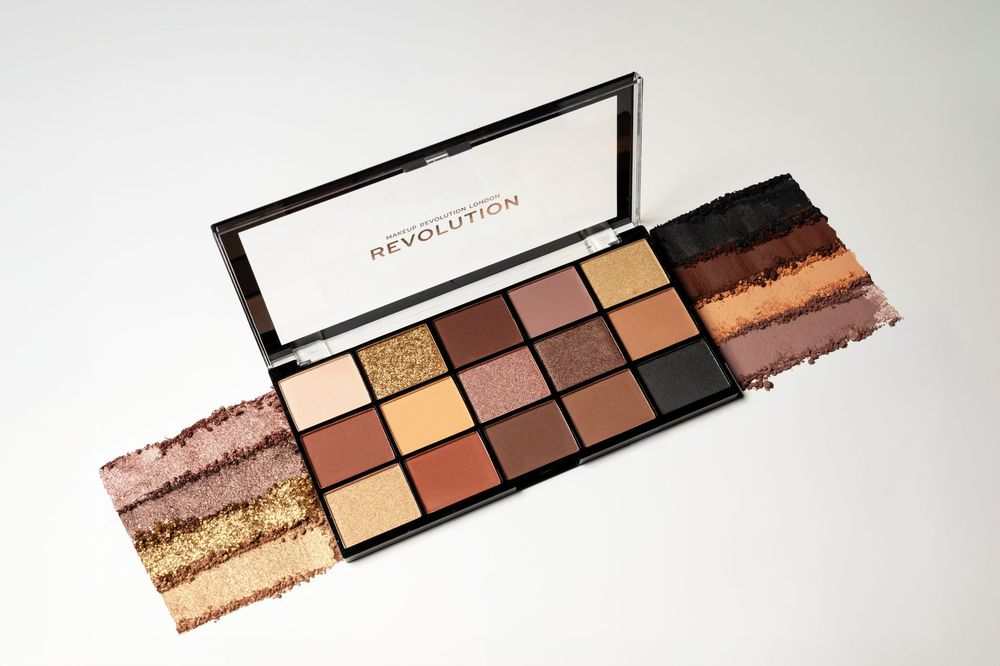 Revolution makeup eyeshadow palette with 15 warm nude shades, displayed open with colorful swatches on white background.