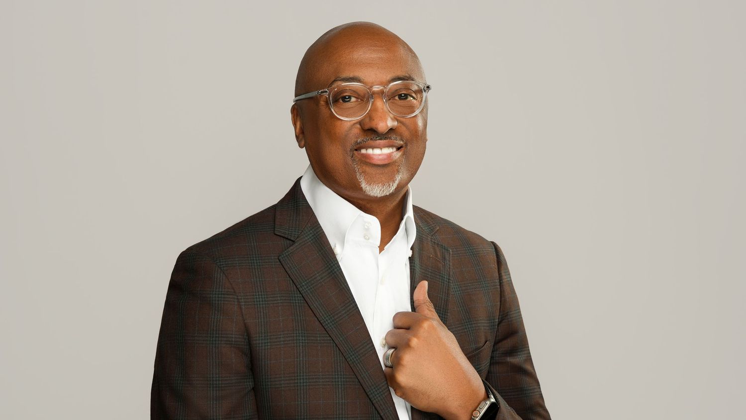Professional headshot of a person in glasses and brown plaid blazer giving thumbs up.